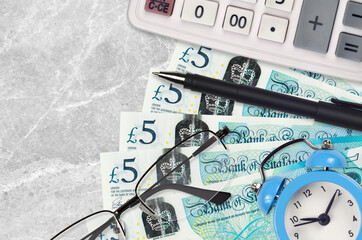 5 British pounds bills and calculator with glasses and pen. Business loan or tax payment season...