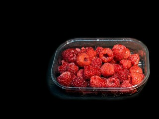 Red raspberries in plastic package / box isolated on black background