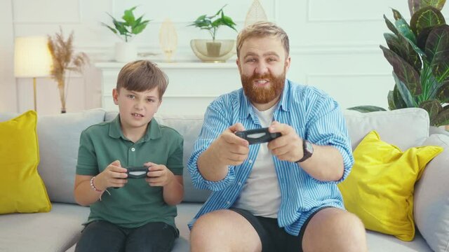Happy bearded father winning the online computer game playing video controller with his son celebrating victory. Home entertainment. Fun concept. Families. Emotions.