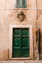 Fototapeta na wymiar Closed double-leaf green wooden doors with patterns under the window and a carved figure in the wall.