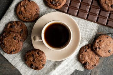 Coffee cup with cookies and chocolate on wooden table background. Mug of black coffee with chocolate cookies. Fresh coffee beans.