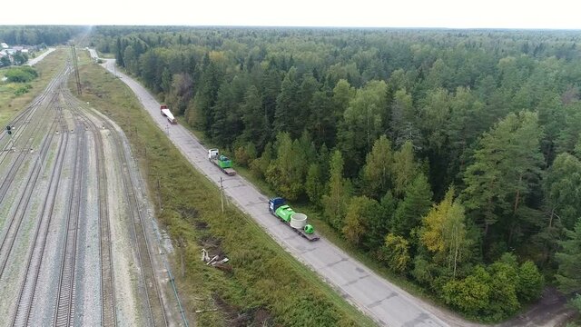 High flight over the motorway and railroad. Cars with a large load are going slowly. Around green forests. Wind turbine transportation.