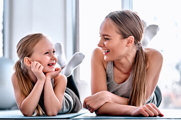 Beautiful young woman and charming little girl are looking at camera and smiling while lying on...