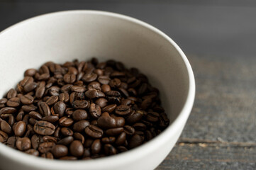Bowl filled of fresh arabica or robusta coffee beans on a wooden table.
