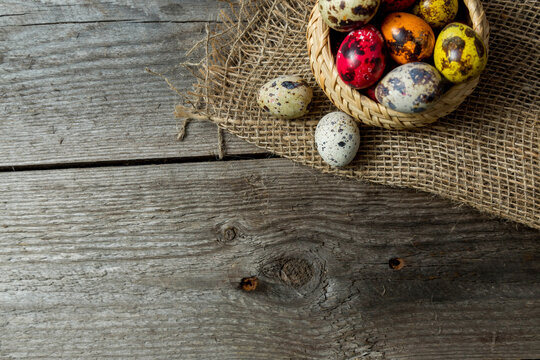 Hand painted easter eggs in wicker basket on burlap napkin on wooden background