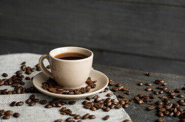Coffee cup with roasted coffee beans on wooden table background. Mug of black coffe with scattered coffee beans on a wooden table. Fresh coffee beans.