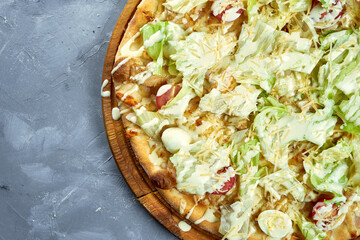 Baked italian pizza with cherry tomatoes, lettuce, parmesan, croutons, chicken on a wooden tray on a gray background. Caesar pizza