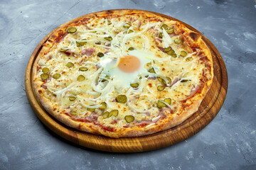 Baked Italian pizza with yolk, parmesan cheese, bacon and creamy sauce on a wooden tray on a gray background.