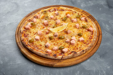 Baked italian pizza with salmon, olives and cheese on a wooden tray on a gray background.