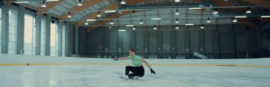 Female ice figure skater falls on ice while practicing jumps on the rink. Shot on RED cinema camera with 2x Anamorphic lens, 75 FPS slow motion