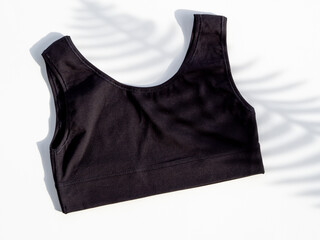 sports bra top view. Black cotton sports bra isolated on white with trendy palm leaf shadow, Flat...