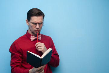 Portrait of thoughtful man in spectacles and copybook, touching his face over blue background