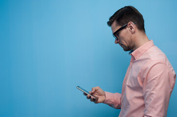 Portrait of a handsome young man in glasses scrolling social media in a smartphone