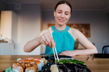 Smiling woman enjoying tasty sushi while spend good time at home sitting at the table in the living room. Focus on sushi rolls
