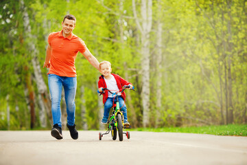 Obraz premium Dad teaches little son to ride bike in park, keep balance, have fun family. Father day concept