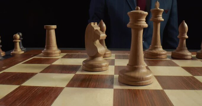 Male hand making move with white horse knight on chess board isolated over black background
