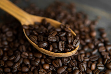 Fresh roasted arabica coffee beans in a wooden spoon and scattered coffee beans on a wooden table.