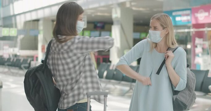 Young Caucasian women in face masks greeting each other in airport at arrival terminal. Conscious female tourists touching elbows to avoid contact. Contactless hello on Covid-19. Cinema 4k ProRes HQ.