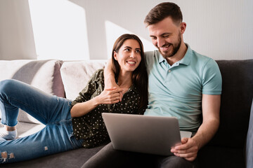 Smiling couple relaxing on the sofa with a notebook hugging each other