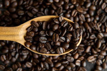 Fresh roasted arabica coffee beans in a wooden spoon and scattered coffee beans on a wooden table.