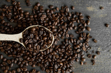 Fresh roasted arabica coffee beans in a wooden spoon and scattered coffee beans on a wooden table.