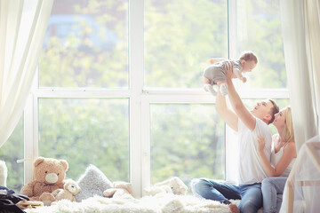 mom dad and baby little toddler sitting on the window / young family in a new apartment, beautiful...