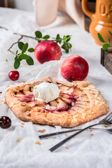 Homemade galette with peaches and ice cream on light background