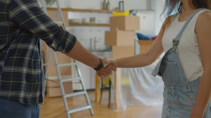 Close up of woman landlord giving keys of apartment to man tenant and shaking hands in agreement