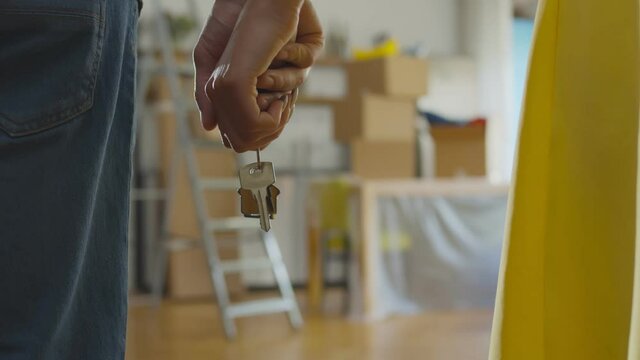 Close up of couple holding hands and keys to new apartment over background with boxes