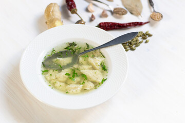 Chiken broth with dough and herbs in plate on white wooden background with spoon and spices
