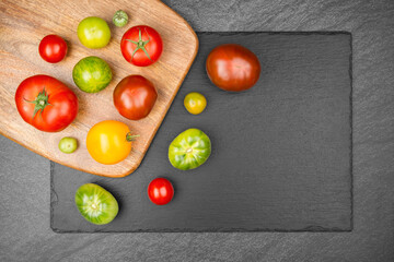 Different sorts of tomatoes on a wooden cutting board which lies on a slate slab. With copy space.