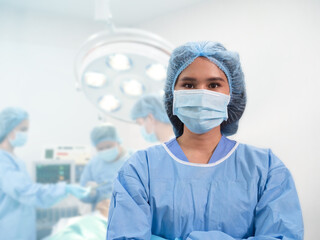 Fototapeta na wymiar Young Asian female surgeon standing with blurry background of the surgeon team in the operation room.