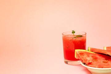 Delicious red watermelon juice with sliced fruit pieces on a plate. A sprig of mint in a glass. Copy space. Summer food concept