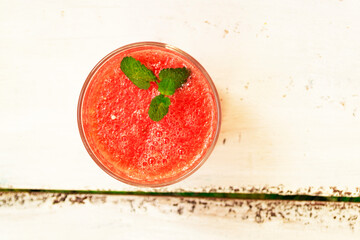 Delicious red watermelon juice with a sprig of green mint in a glass glass on a white background. Copy space. Summer food concept.