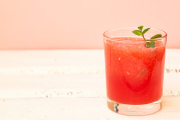Delicious red watermelon juice with a sprig of green mint in a glass glass on a white background. Copy space. Summer food concept.