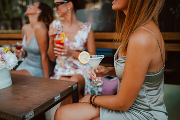 Three beautiful young caucasian women in short summer dresses are sitting and drinking cocktails in the cafe garden. Girls at parties