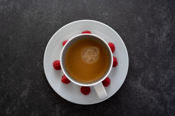 Top down view of cup filled with coffee placed on a white plate decorated with red raspberries