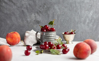 Fresh cherries in a metal vintage mug and peaches on the table