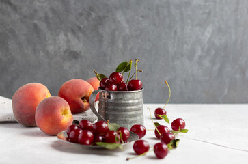 Naklejka na ściany i meble Fresh cherries in metal vintage mug and peaches, copy space