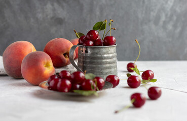 Naklejka na ściany i meble Fresh cherries in a metal vintage mug and peaches on the table