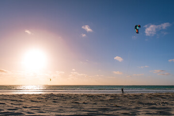 Silhouette of kitesurfer over sunset sky. Surfer holding kite on the beach. Freestyle kiteboarding