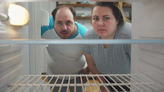 Overweight young couple on diet looking in empty fridge