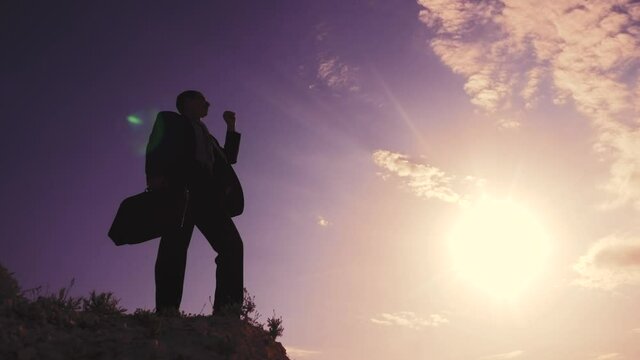 business success teamwork concept. man businessman in a jacket with a silhouette suitcase rises to the top of mountain looks into the distance, shows hand direction. manager head set a lifestyle goal