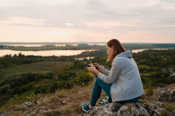 Young Caucasian woman navigating a flying drone with remote control with a picturesque landscape in background