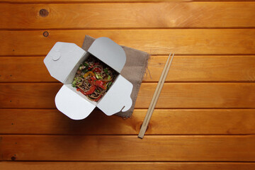 wok box and chopsticks isolated on canvas napkin on wooden table flat lay