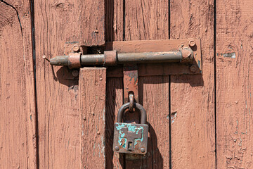 Old rusted grungy wooden garage door with latch and padlock. Close up of rusty vintage lock on...