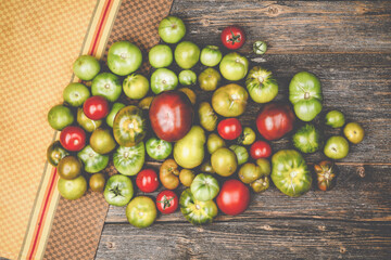 Heap of different sorts of tomatoes on a wooden table with dish towel