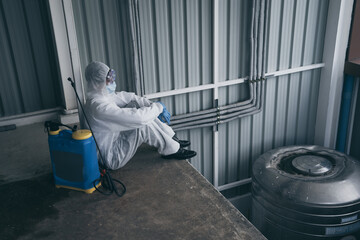 Man in virus protective suite and mask tired or rest while cleaning covid19 infected area, Virus disinfection concept