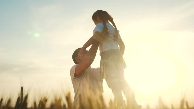 happy family dreams concept. father throws daughter up playing in the field with wheat silhouette. dad play with a little girl kid. friendly family holding a child lifestyle together