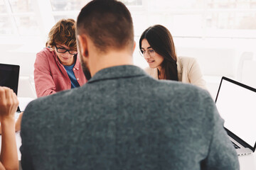 Crew of skilled male and female marketing expert creating advertising content for increasing rating of web magazine popularity using laptop computer and wireless connection cooperating in office